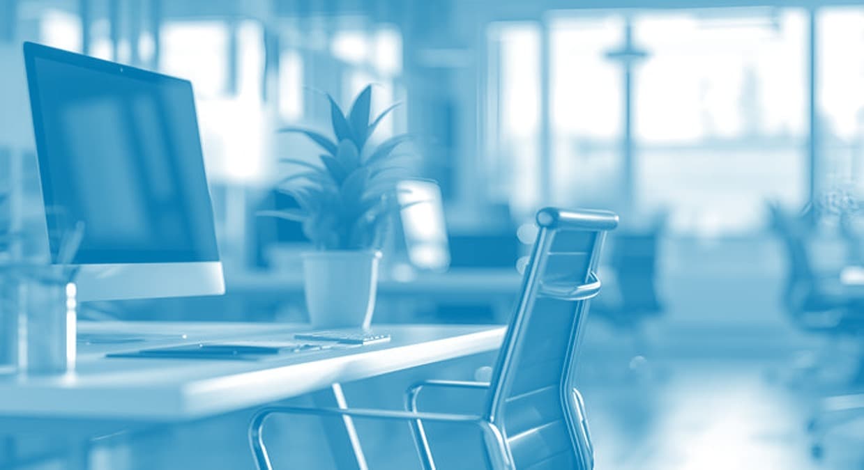 A quiet enterprise workspace with a monitor, desk and office chair beside a daylit window